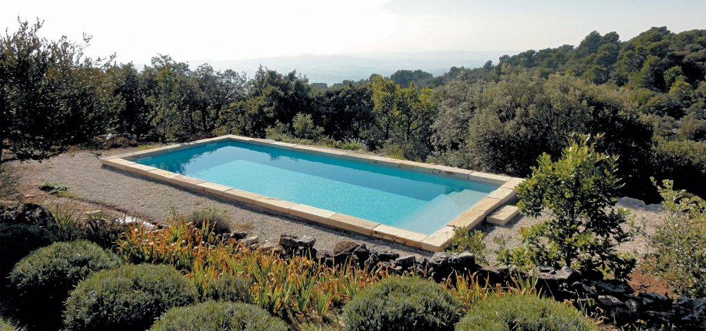 Piscine rectangulaire dans un cadre naturel avec vue sur les montagnes, entourée d'une terrasse en pierre et de végétation méditerranéenne.