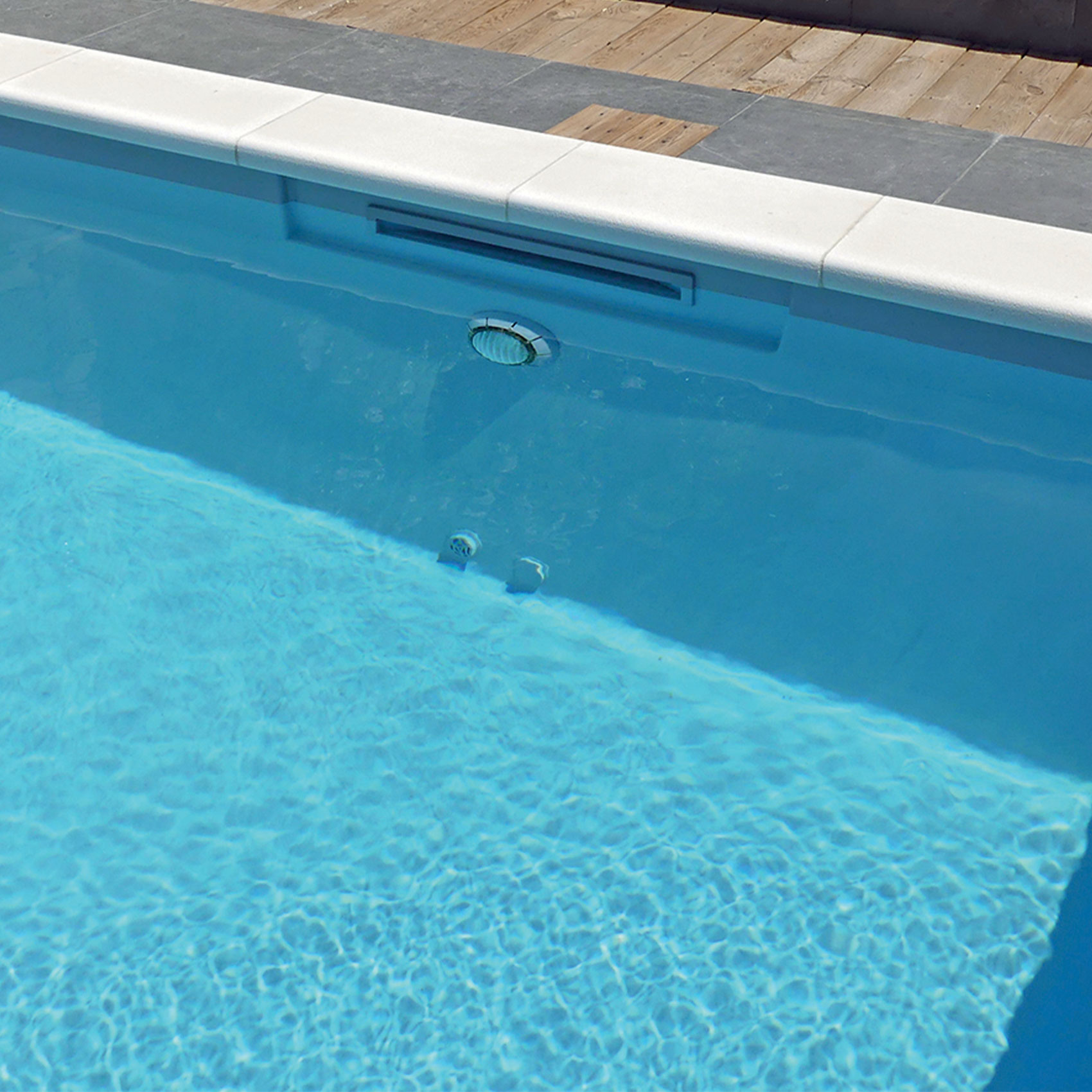 Piscine moderne à débordement avec eau bleu clair et bordure en bois et carrelage blanc.