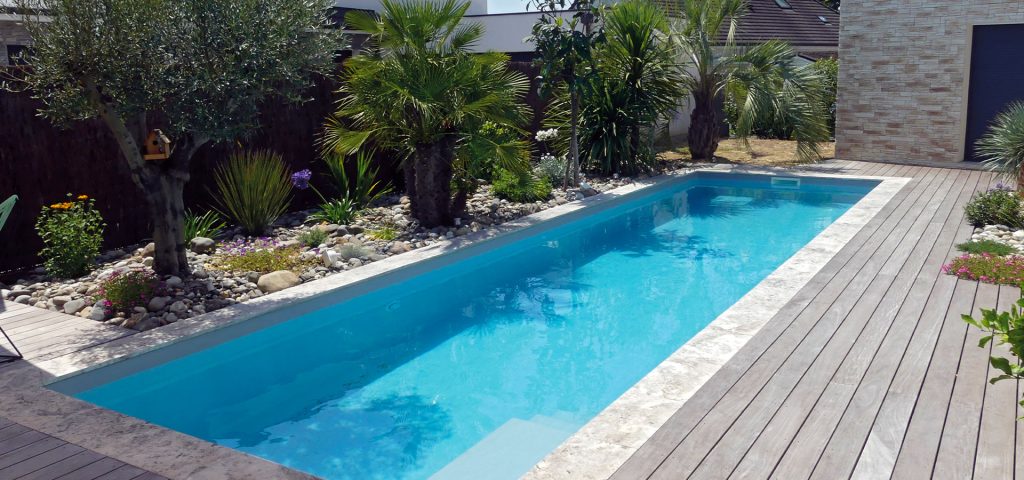 Piscine rectangulaire extérieure avec terrasse en bois et jardin paysager exotique.