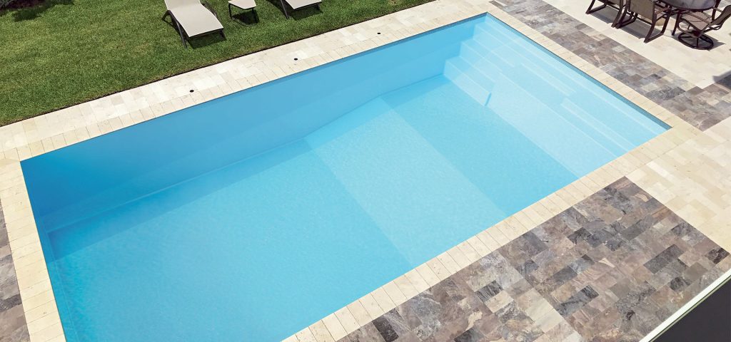 Description pour la balise alt SEO : "Piscine rectangulaire moderne avec eau cristalline entourée de carrelages en pierre et d'une zone de relaxation avec chaises longues et pelouse verte"